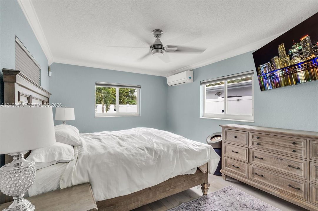 Bedroom featuring crown molding, dual-pane sliding windows, ceiling fan, and a wall-mounted ductless air conditioning unit