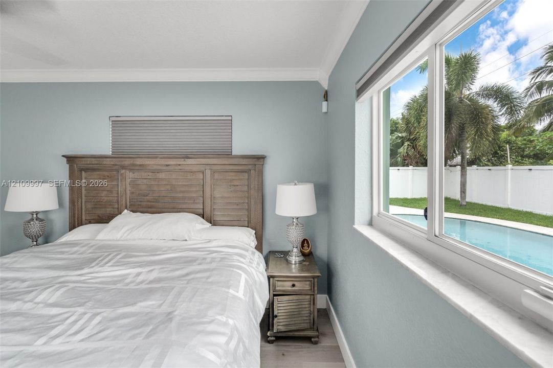Interior space featuring crown molding, neutral wall color, wood-finish flooring, and a large window with stone sill, showcasing an exterior swimming pool and fenced yard