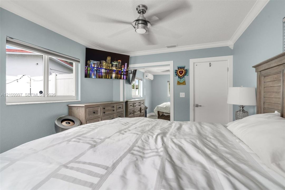 Bedroom featuring crown molding, a brushed-nickel ceiling fan, double-pane windows, and a wall-mounted climate control unit