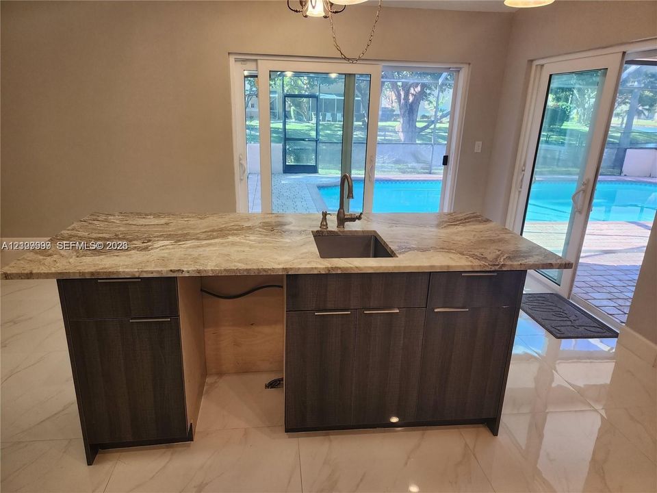 Kitchen island with stone-surface countertop, under-mount sink, high-arc faucet, and dark-finish cabinetry