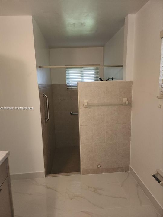 Walk-in shower featuring neutral tile surround, metal grab bars, built-in recessed shelf, and light-toned tile flooring
