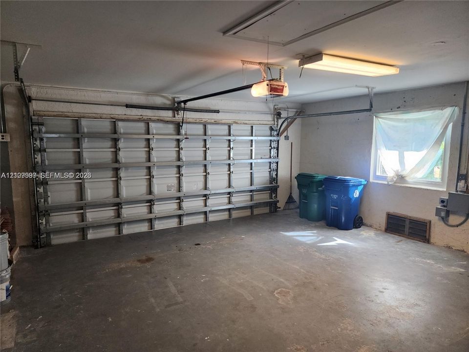 Enclosed garage featuring a multi-panel overhead door, automatic door opener, fluorescent overhead lighting, and an exterior window
