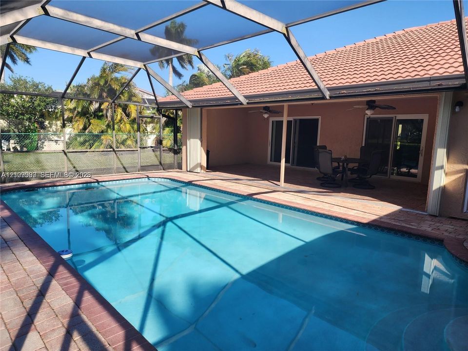 Screen-enclosed swimming pool with a concrete pool deck, covered patio, and tiled roof