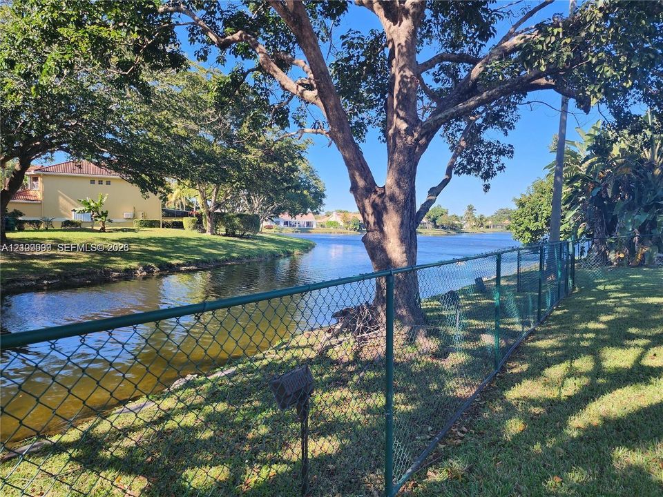 Waterfront lot featuring mature trees, a chain-link perimeter fence, and grass landscaping