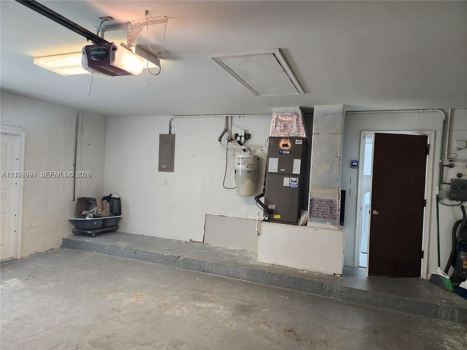 Garage featuring concrete flooring, an overhead automatic door opener, a dedicated HVAC unit, an electrical panel, and an access door