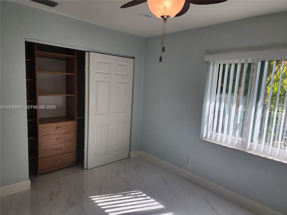 Room featuring large-format tile flooring, a custom-built wood closet system with integrated shelving and drawers, a ceiling fan with integrated lighting, and vertical window blinds