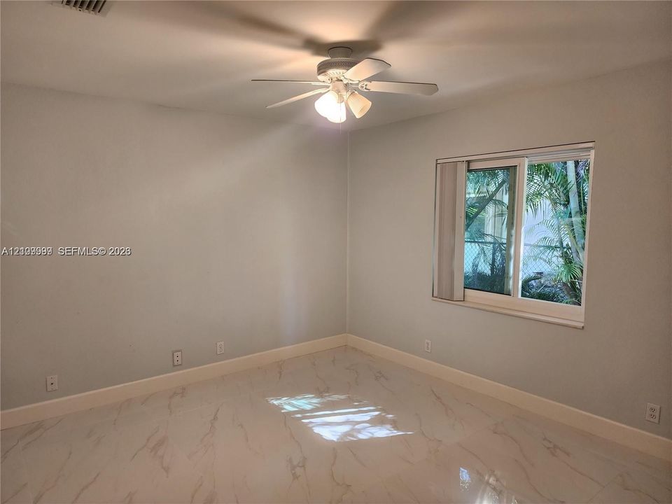 Neutral interior featuring polished stone-finish flooring, a ceiling fan with integrated light fixture, and a sliding window