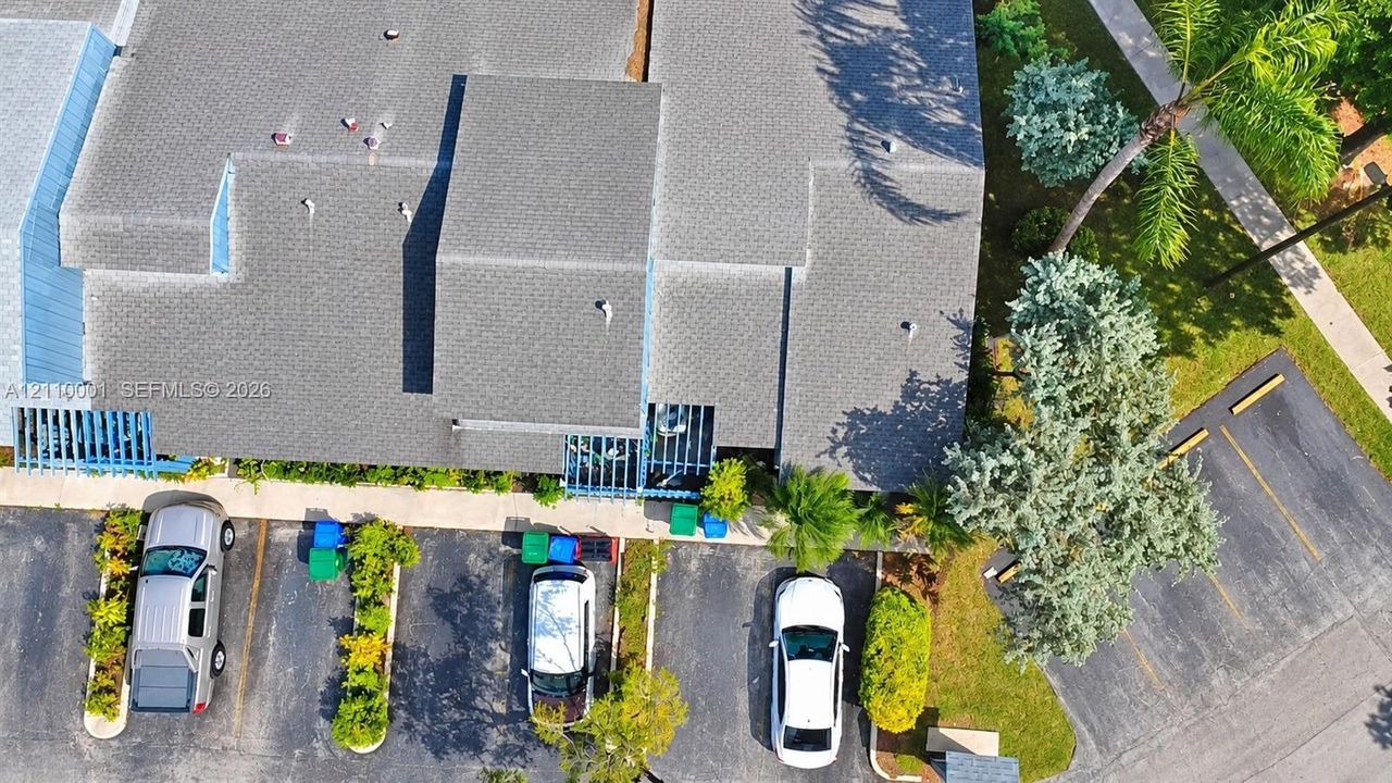 Aerial perspective of property featuring shingled roof lines, blue structural lattice accents, paved parking area, and mature landscape elements