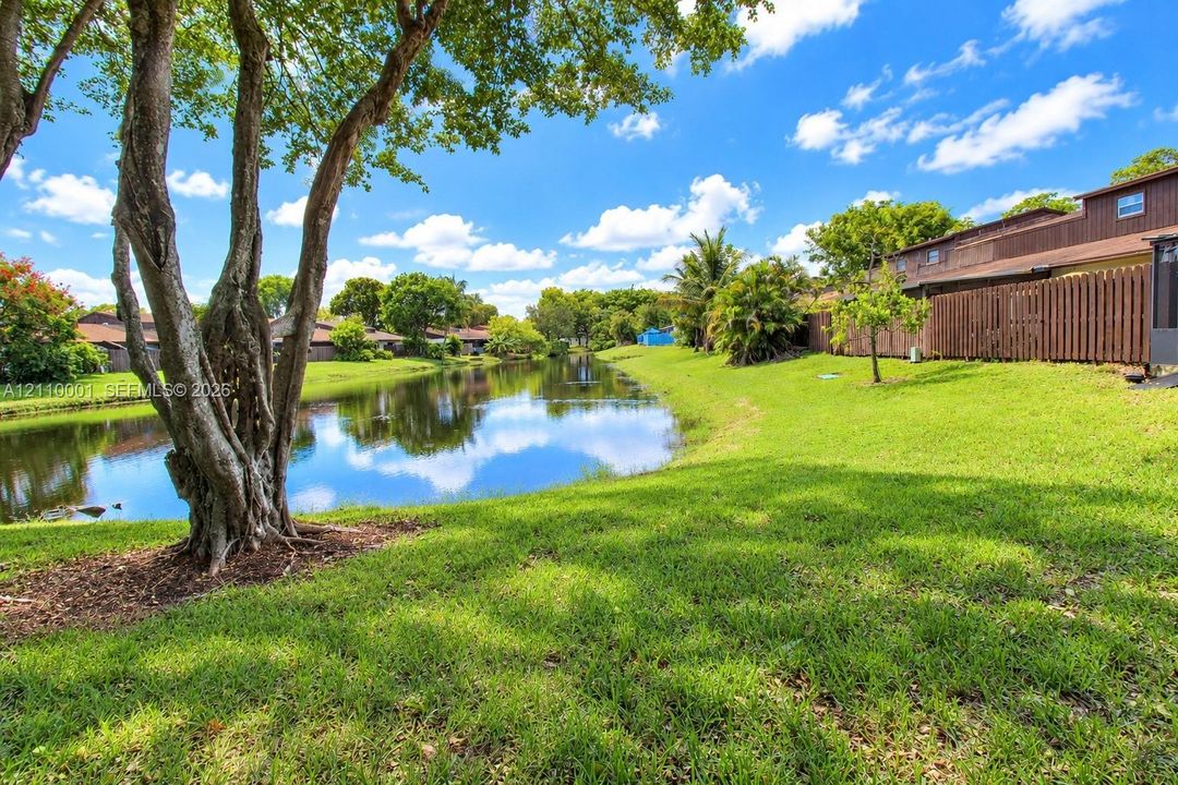 Waterfront backyard featuring a manicured lawn, mature trees, and a wooden perimeter fence