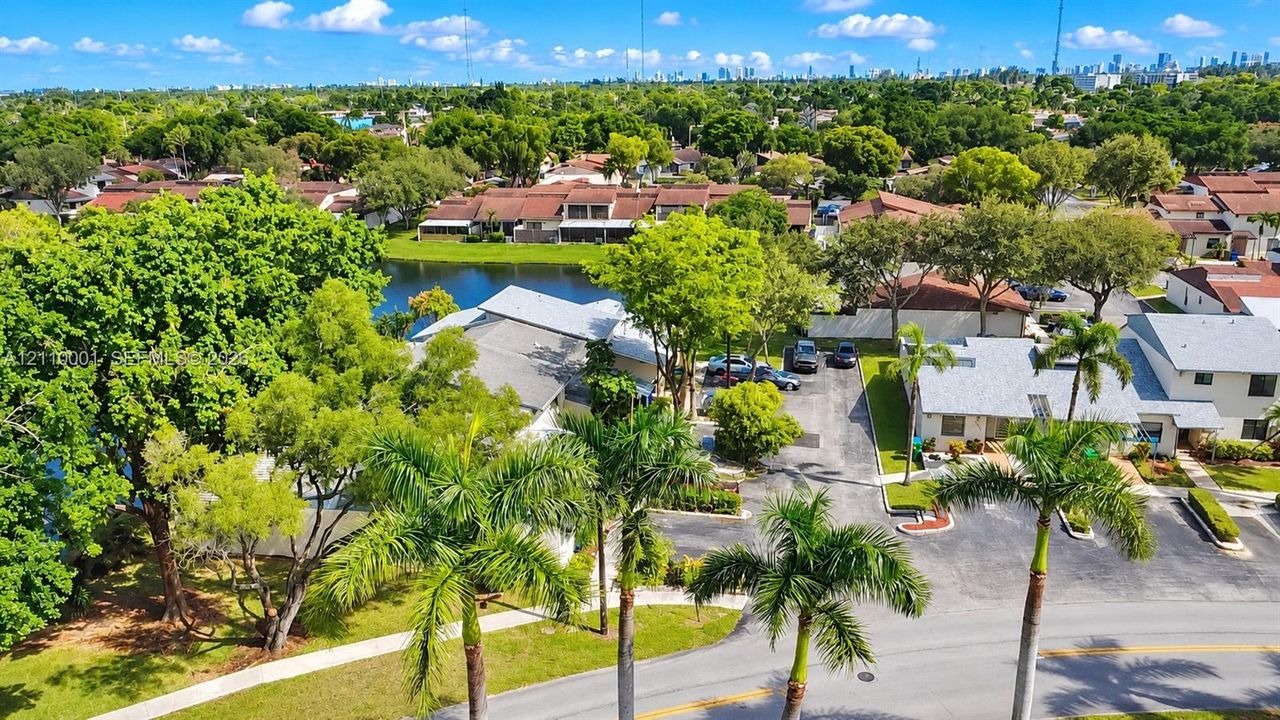 Aerial perspective featuring palm-lined streets, mature trees, a central lake, and multi-unit residential structures