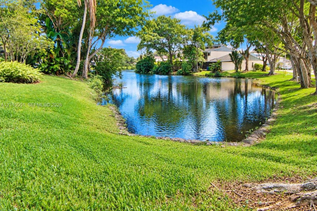 Waterfront lot featuring a manicured lawn, stone-lined pond edge, and mature trees