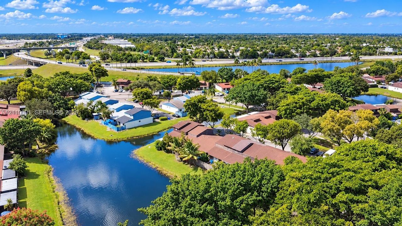 Aerial perspective of a multi-unit residential property featuring waterfront positioning, expansive green space, mature landscaping, and brown shingle roofing