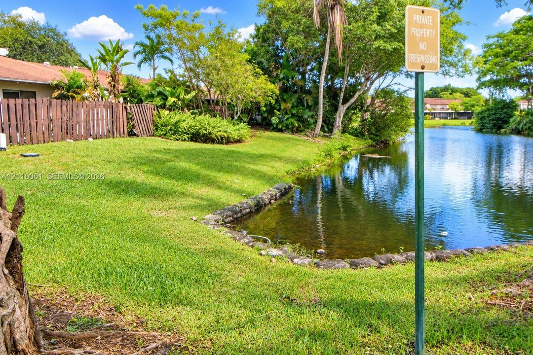 Waterfront lot featuring a natural grass lawn, stone-lined bulkhead, mature trees, and wooden perimeter fencing