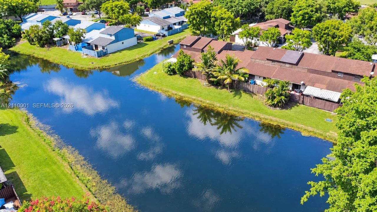 Aerial perspective featuring a waterfront pond, manicured lawn, and mature canopy trees