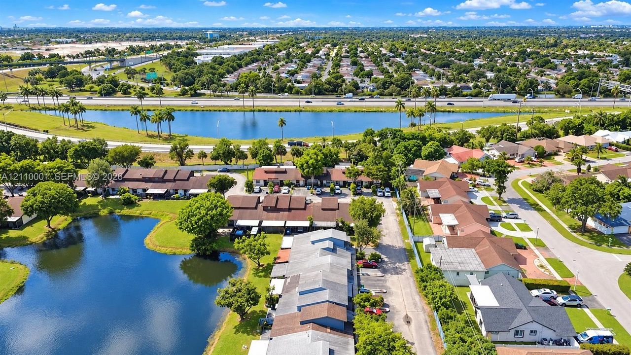 Aerial perspective featuring multi-unit structures, water frontage, landscaped greenery, and paved parking areas
