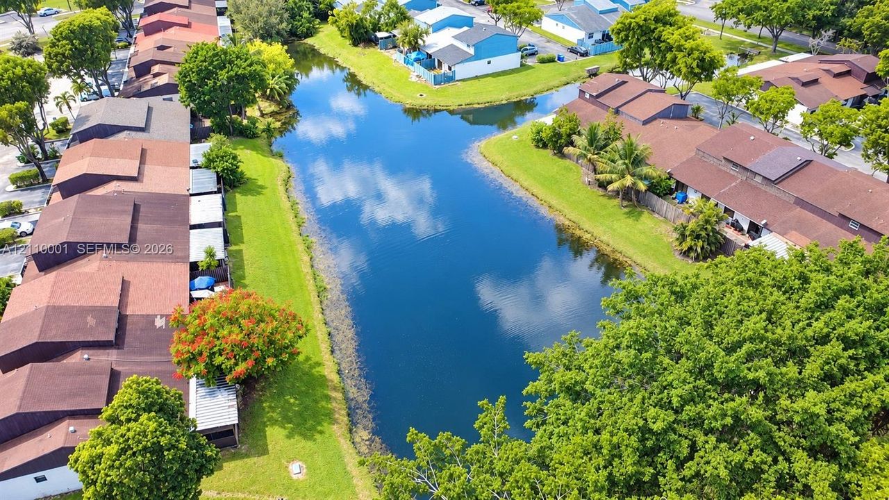 Aerial perspective of a multi-unit residential complex featuring a central canal, mature trees, and manicured green spaces