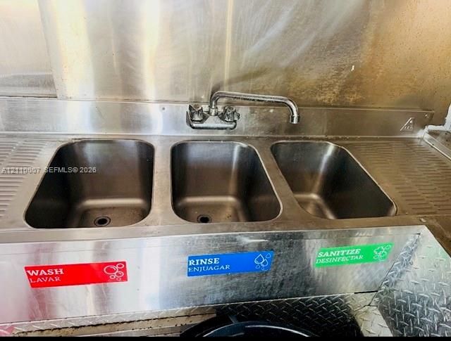 Commercial-grade stainless steel triple-basin sink featuring an integrated backsplash and wall-mounted metal faucet