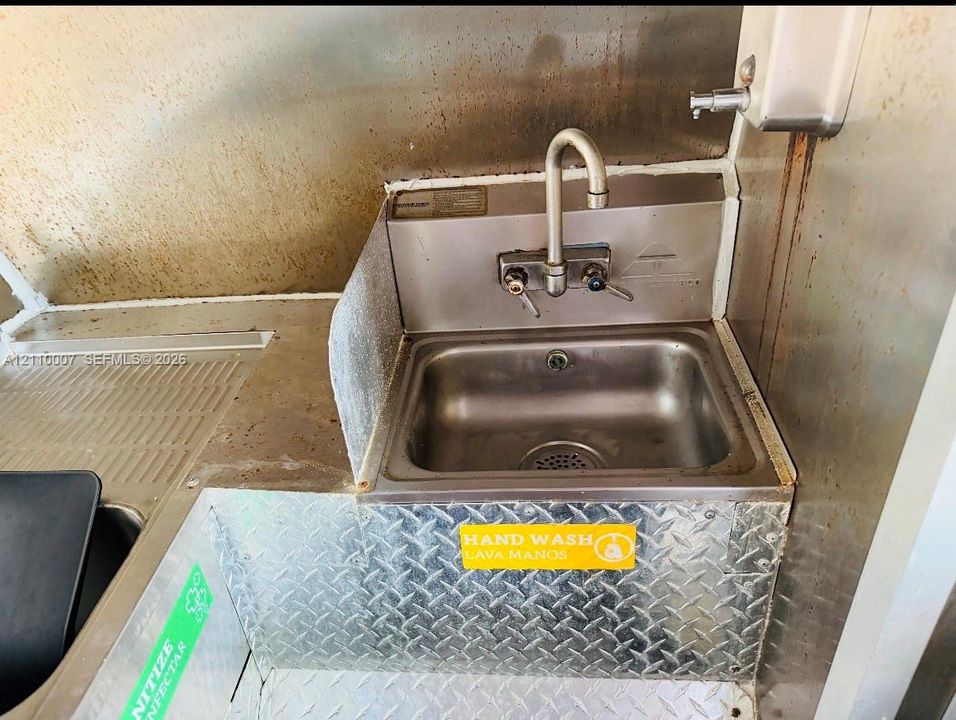 Stainless steel utility sink with a gooseneck faucet, integrated metal backsplash, diamond-plate metal cabinetry, and a wall-mounted soap dispenser
