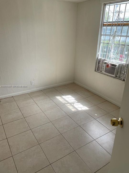 Interior room featuring neutral ceramic tile flooring, textured wall finishes, and a window equipped with decorative security bars
