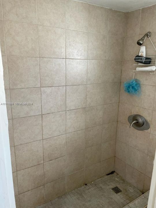 Walk-in shower featuring floor-to-ceiling neutral ceramic tiling, a single-handle brushed metal faucet, and an overhead shower head