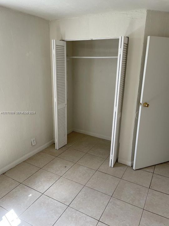 Interior space featuring neutral-toned tile flooring, a closet with bi-fold louvered doors, and a standard swinging door with a brass-finish knob