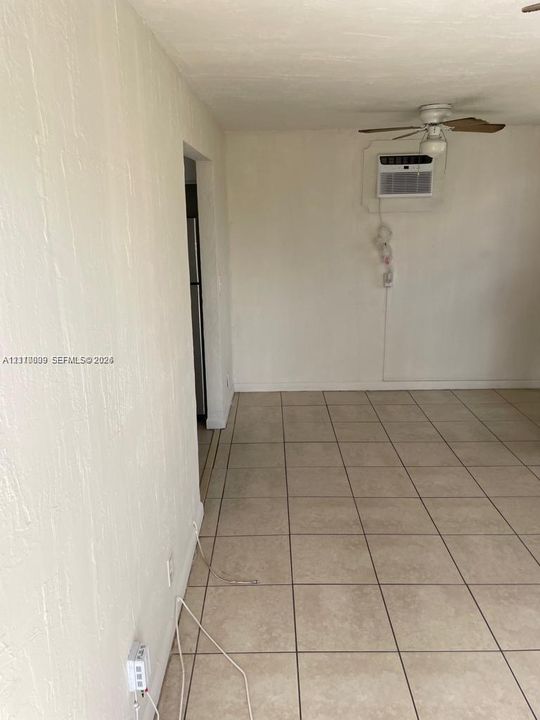 Interior space featuring light-toned ceramic tile flooring, a mounted wall air conditioning unit, and a ceiling fan