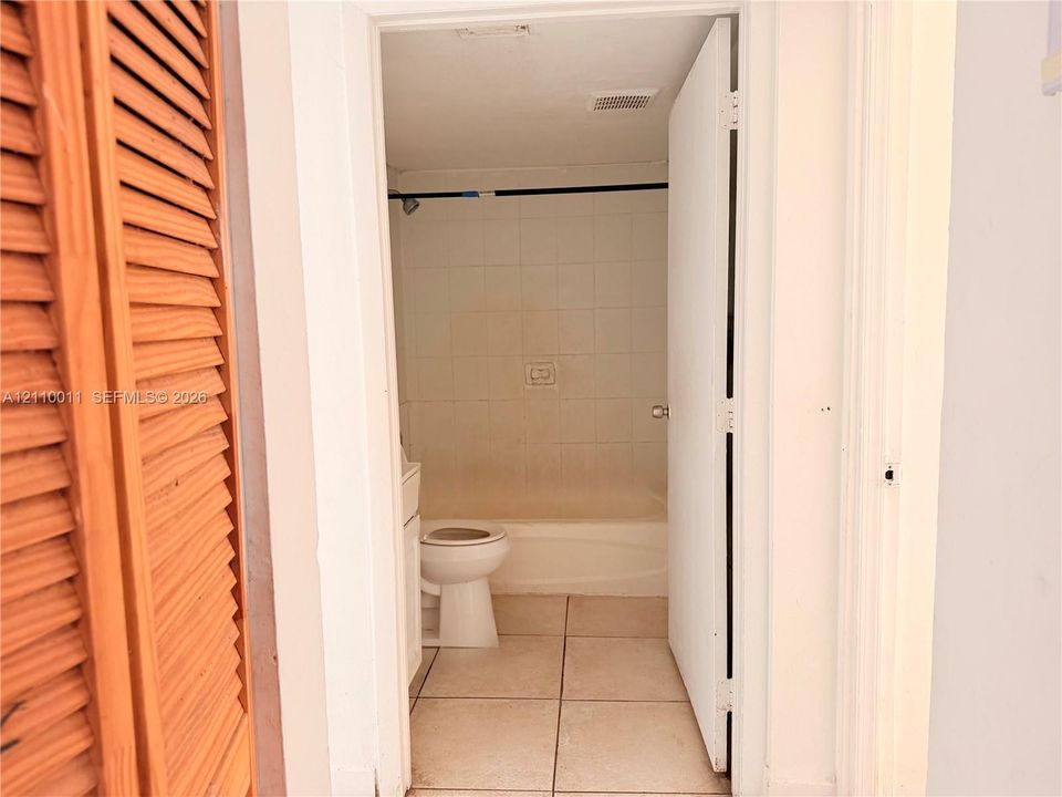 Bathroom featuring white tile wall surround, standard soaking tub, floor-to-ceiling tile flooring, and wood-slat bi-fold door