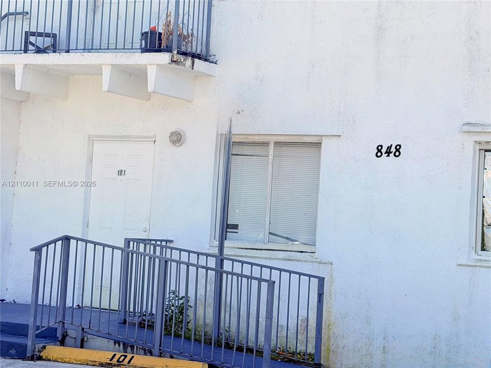Stucco exterior featuring a white door, metal railings, and a ramp