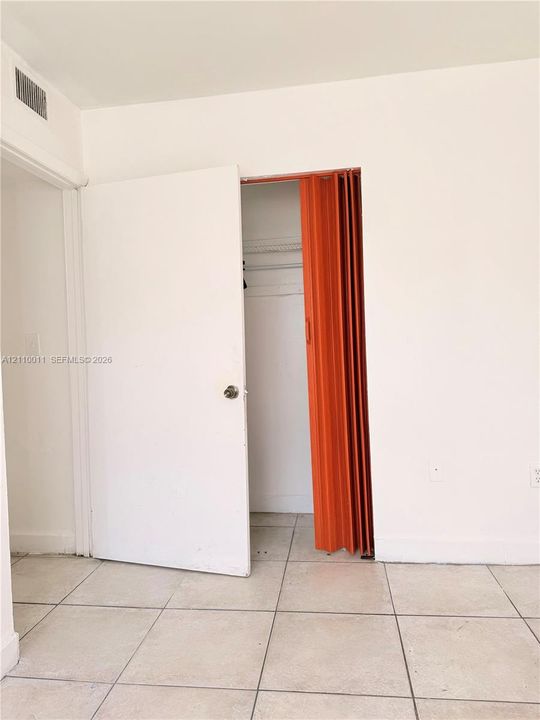 Ceramic tile flooring throughout, closet featuring a combination of a hinged door and an accordion partition, and a built-in wire shelving system