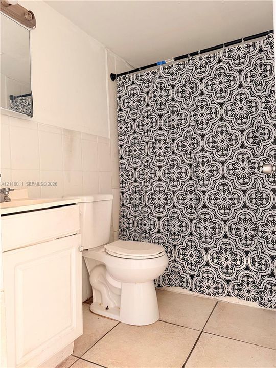 Bathroom featuring white cabinetry, ceramic tile flooring, and wall-mounted vanity lighting