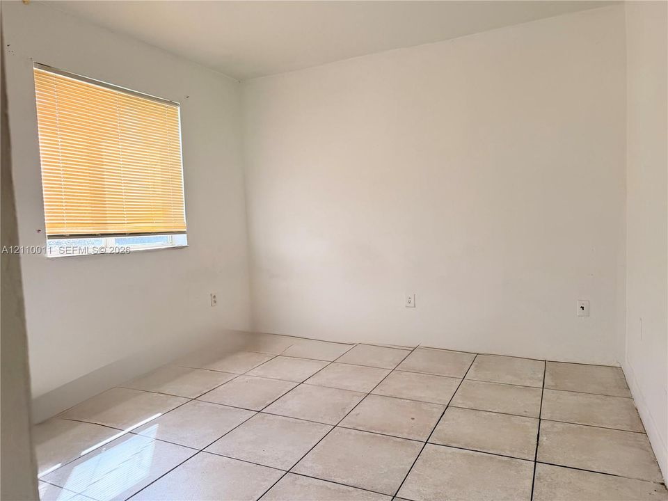 Neutral wall finishes, light-toned ceramic tile flooring, and a single-pane window with attached horizontal blinds