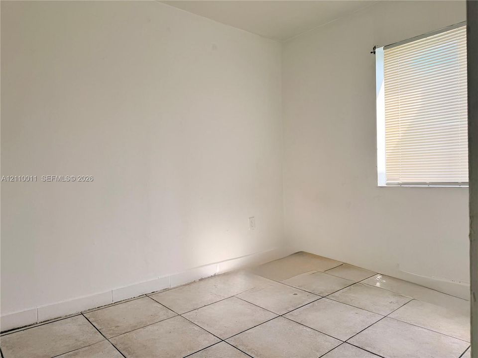 Neutral-toned tile flooring and single window with horizontal blinds