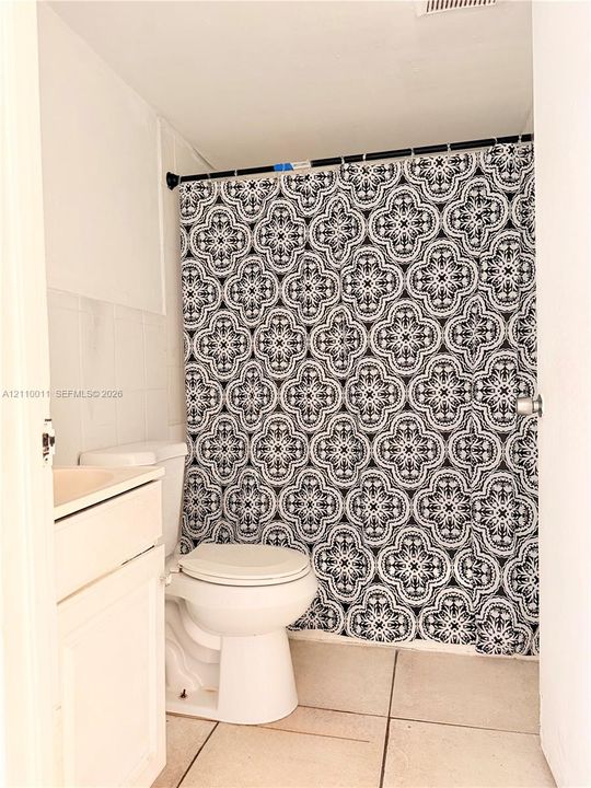 Solid-surface vanity, white ceramic toilet, tile flooring, and neutral wall tiling