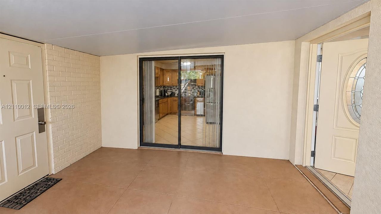 Covered patio featuring ceramic tile flooring, a painted brick accent wall, and sliding glass door entry