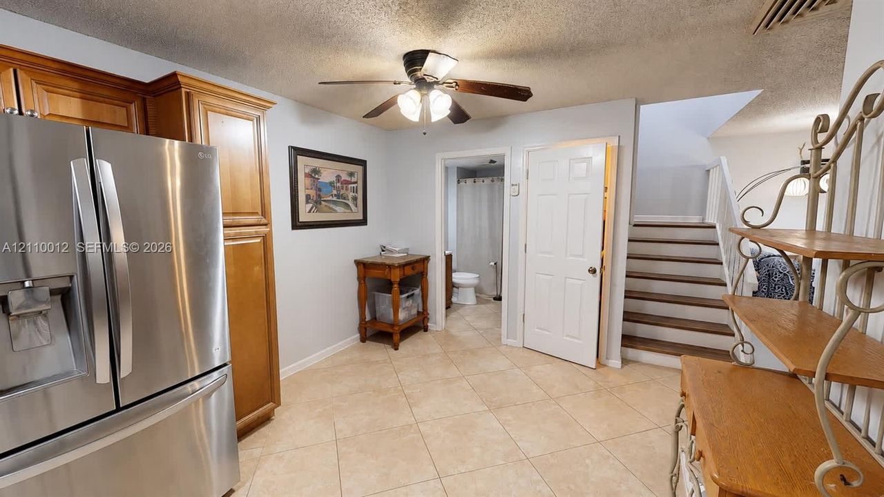 Kitchen area featuring a stainless steel refrigerator, wood cabinetry, ceiling fan, and tile flooring