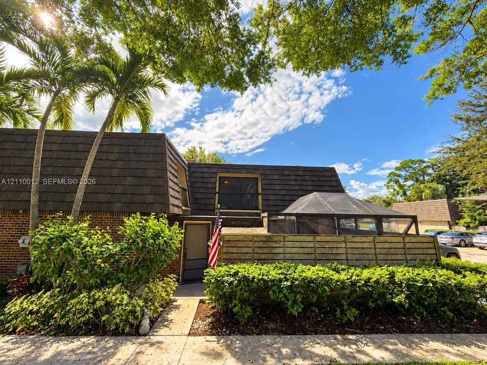 Exterior featuring brick masonry, dark shingled mansard roofline, screened-in enclosure, and mature landscaping