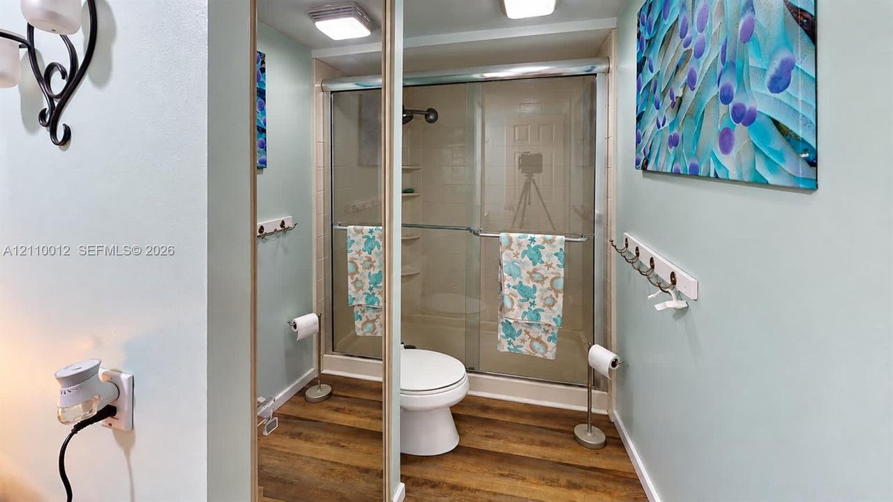 Bathroom featuring wood-finish flooring, a glass-enclosed shower, a wall-mounted hook rack, and overhead lighting