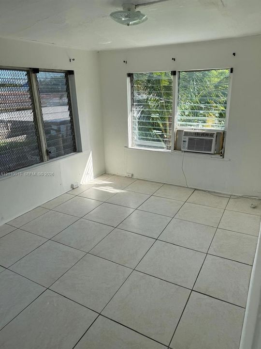 Interior space featuring light-colored ceramic tile flooring, multiple windows with jalousie glass panes, and a mounted ceiling light fixture