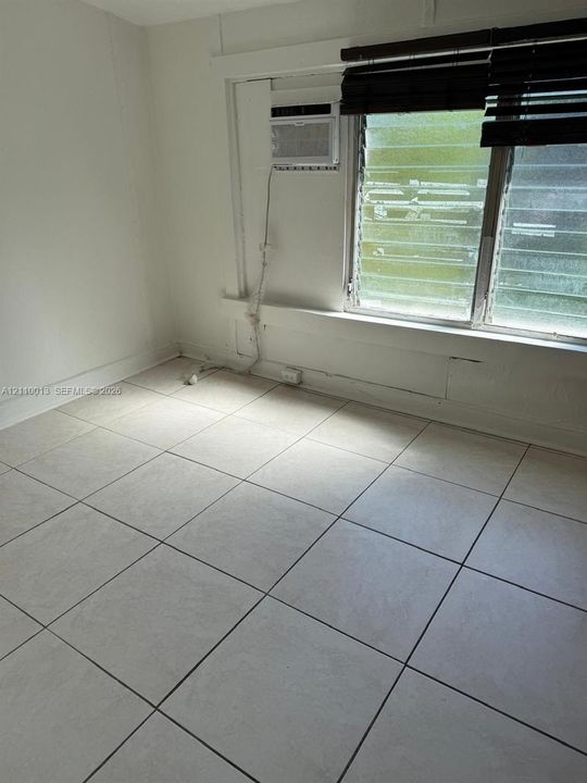 Room featuring light-toned tile flooring, louvered glass windows, and a wall-mounted air conditioning unit