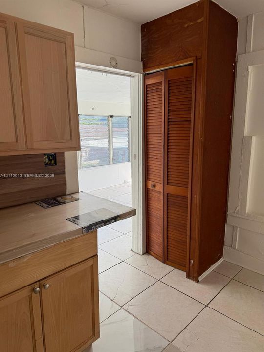 Kitchen featuring wood cabinetry, light-toned countertops, tile flooring, and a floor-to-ceiling wooden bifold pantry
