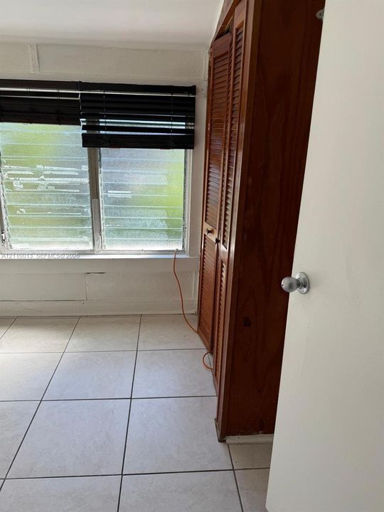 Room featuring large-format tile flooring, built-in wooden closet with louvered doors, and jalousie windows