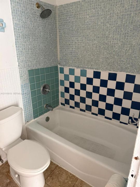 Bathroom featuring a built-in tub with a checkerboard and grid-patterned tile surround, a wall-mounted shower head, metal plumbing fixtures, and tile flooring