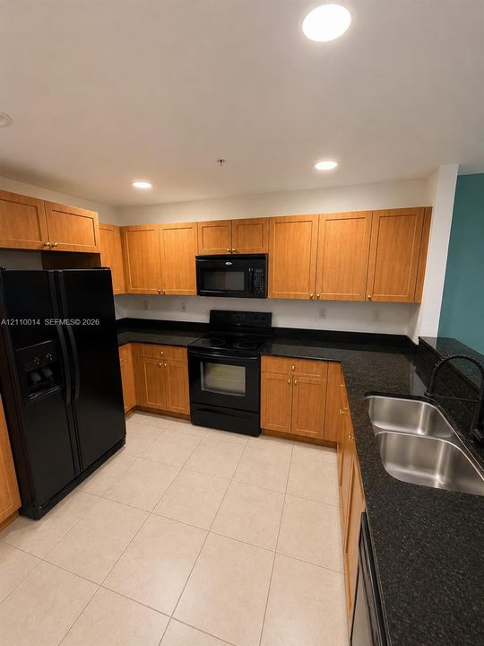 Kitchen featuring flat-panel wood cabinetry, black appliances, dark stone-finish countertops, dual-basin stainless steel sink with high-arc faucet, and tiled flooring