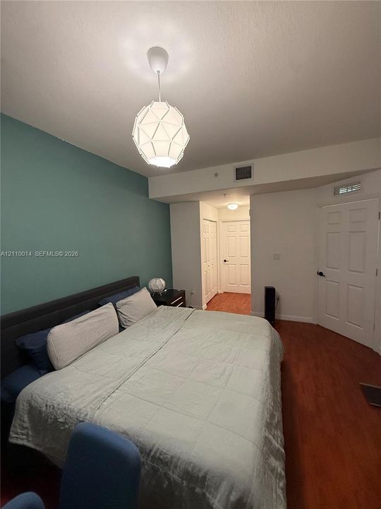 Room featuring wood-finish flooring, a geometric pendant light fixture, and a teal accent wall