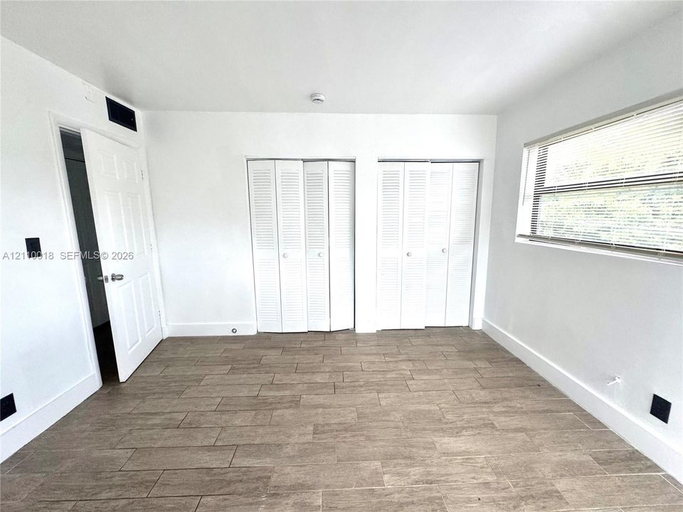 Interior room featuring wood-finish tile flooring, two sets of white louvered-door closets, and a large window with horizontal blinds
