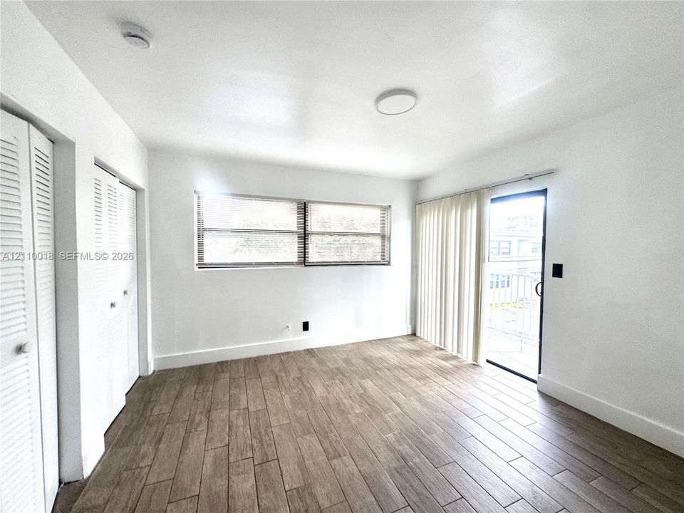 Interior space featuring wood-finish tile flooring, dual louvered-panel closets, horizontal sliding windows, and a glass-paned sliding door