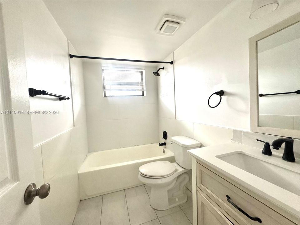 Full bathroom featuring a white porcelain tub with matte black shower hardware, light-toned shaker-style vanity with a solid-surface countertop, rectangular undermount sink, and matte black fixtures