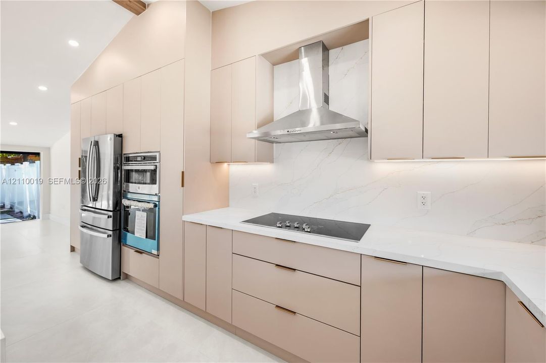 Custom flat-panel cabinetry, stone-surface countertops, full-height stone backsplash, stainless steel built-in double wall ovens, and stainless steel chimney range hood