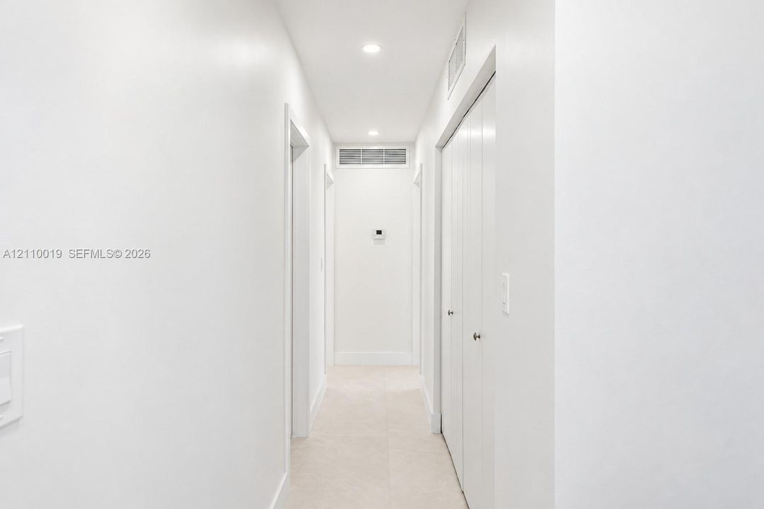 Hallway featuring neutral tile flooring, recessed lighting, and white bi-fold closet doors