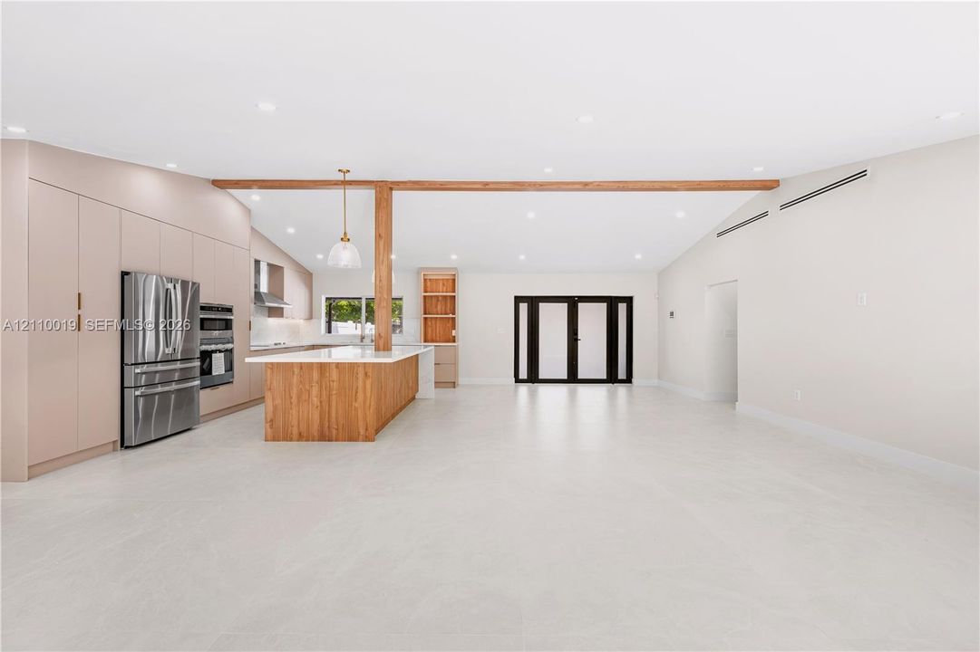 Open-concept kitchen featuring full-height flat-panel cabinetry, a wood-finish island with integrated storage, stainless steel appliances, a structural wood beam, and light-toned tile flooring